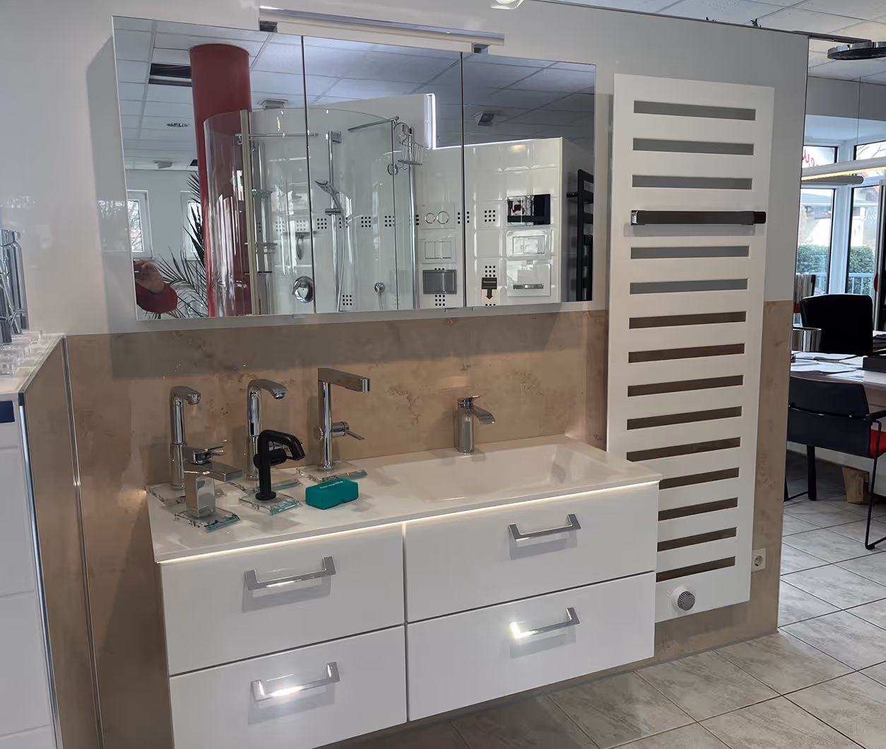 Moderne Badezimmerarmaturen und Waschbecken auf weißem Unterschrank vor Wand mit beige Säule und großem Spiegel.