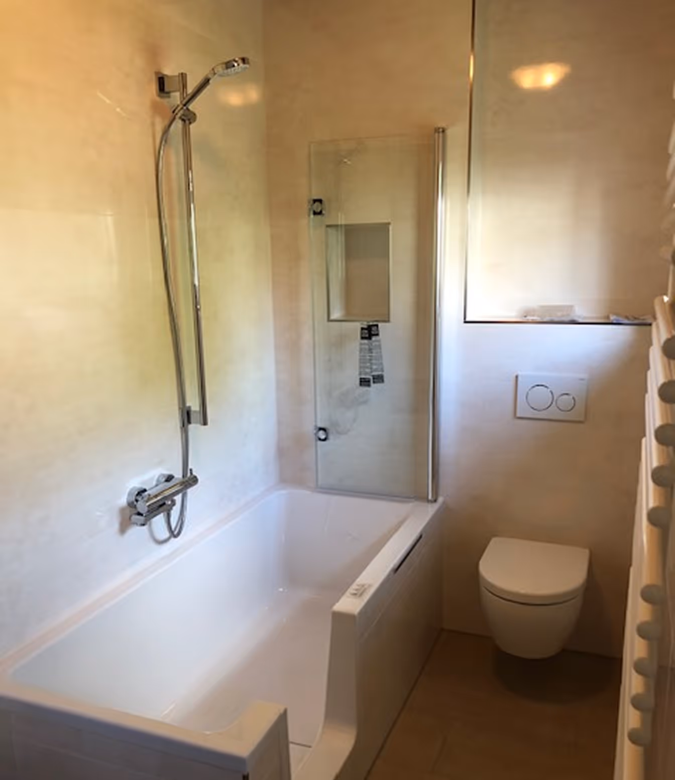 Modernes Badezimmer mit einer weißen Badewanne mit Duschkopf und einer Wandtoilette mit Spülknöpfen.