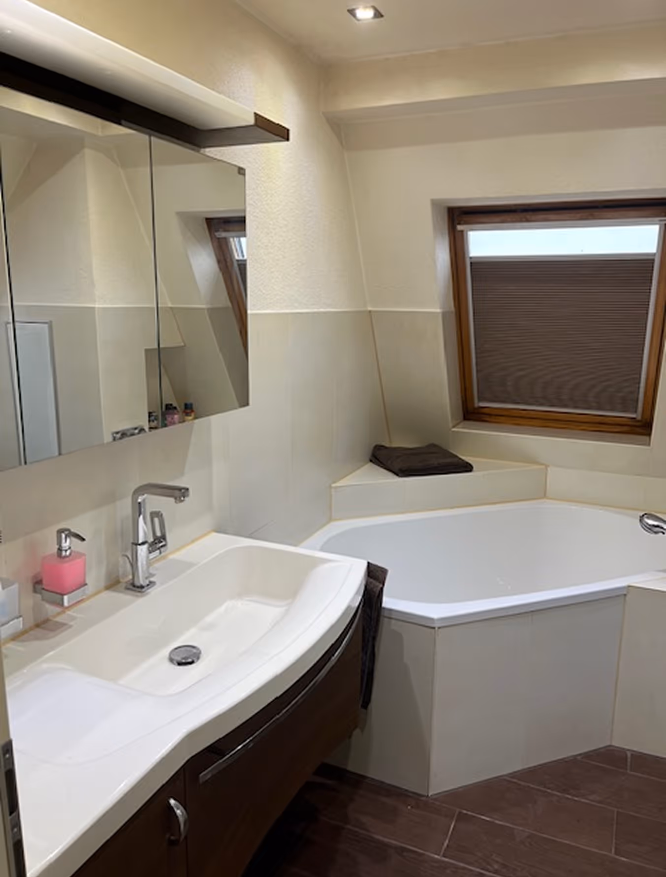 Modernes Badezimmer mit eingebauter Badewanne, Waschbecken mit Spiegel und Fenster mit Jalousie.